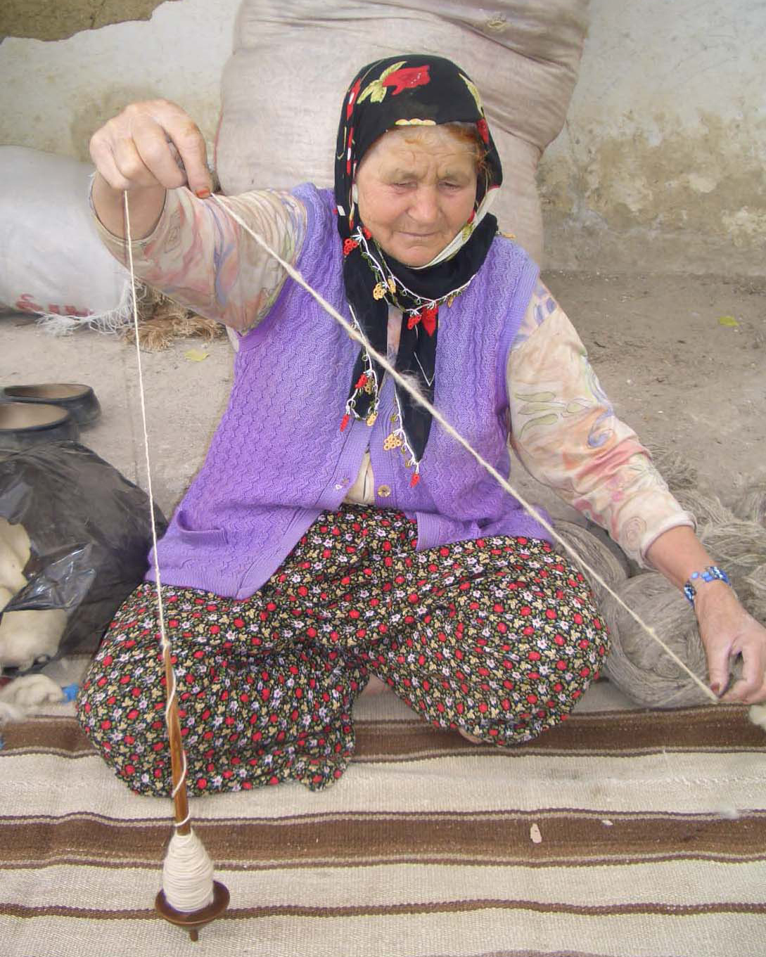 コマを使い糸を紡ぐ織り手の女性の写真